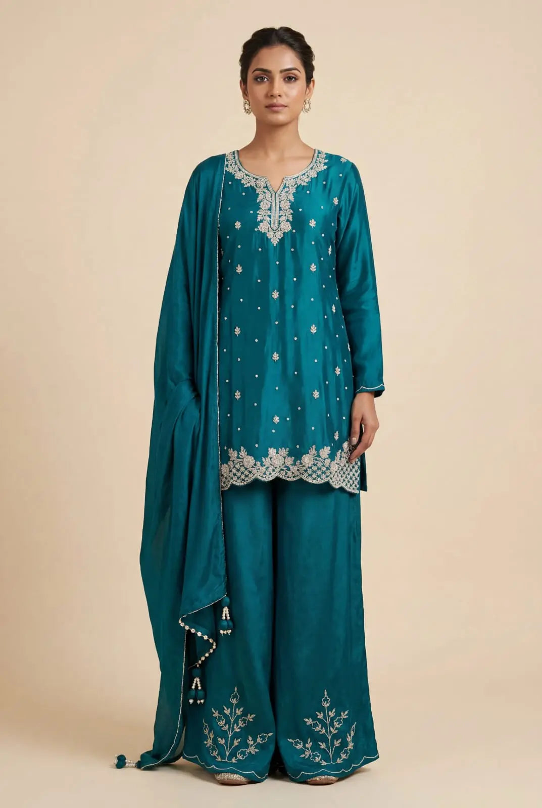 Woman wearing a teal embroidered outfit on a beige background
