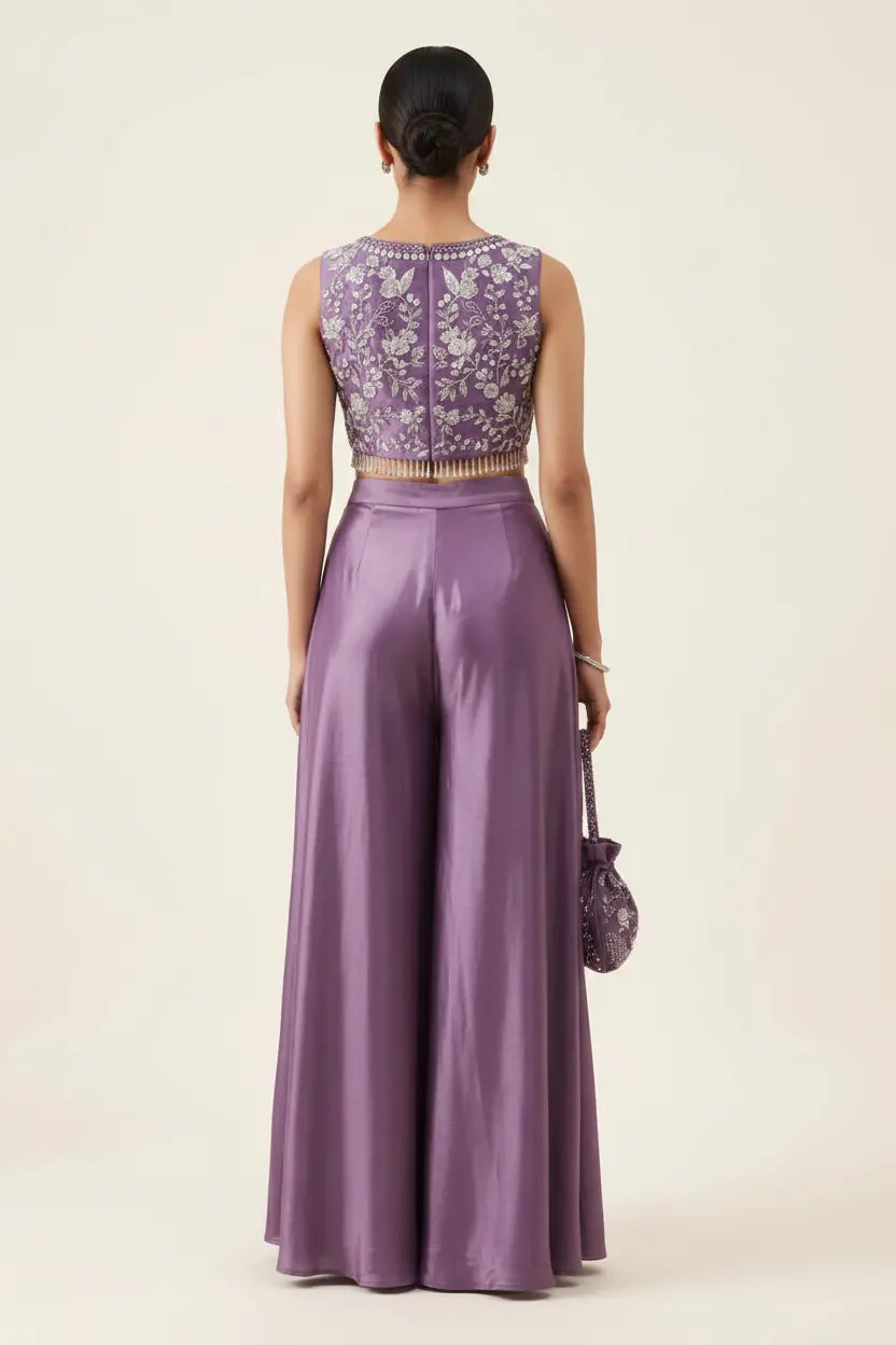 Woman wearing a purple outfit with a matching top and wide-leg pants on a beige background