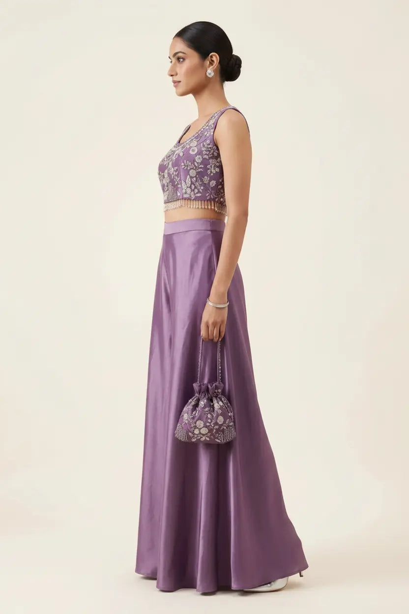 Woman wearing a purple outfit with floral top and skirt, holding a matching bag on a beige background