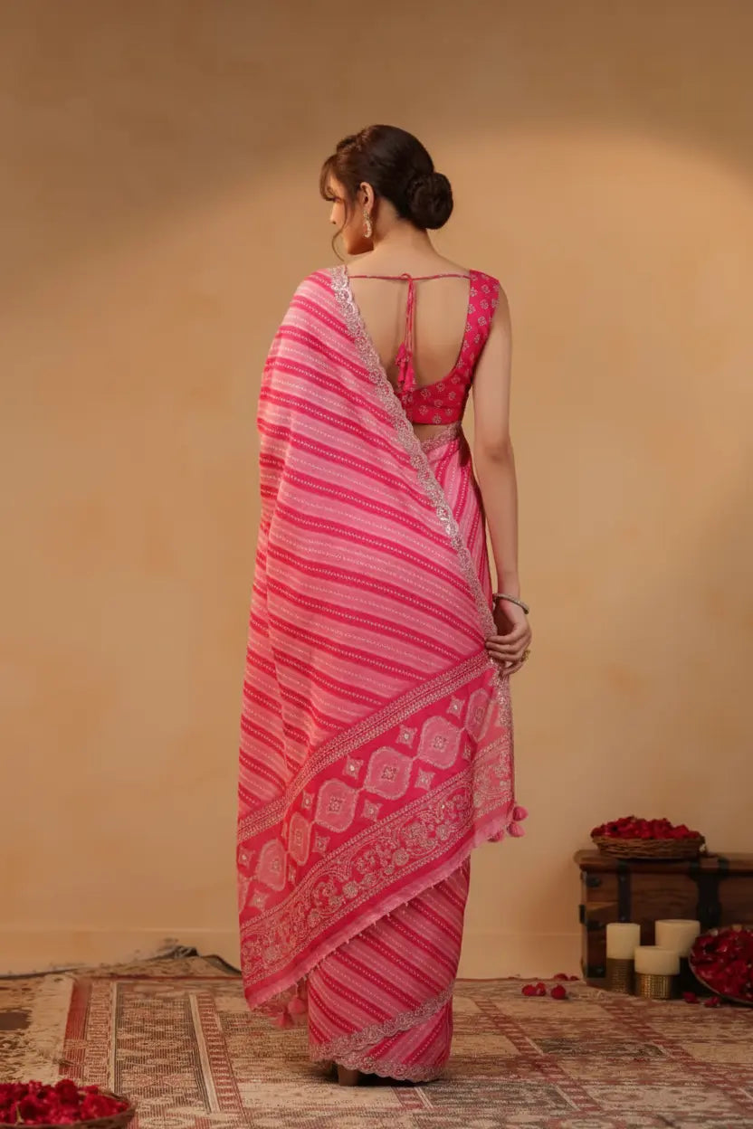 Woman wearing a pink saree with a patterned border against a beige wall.
