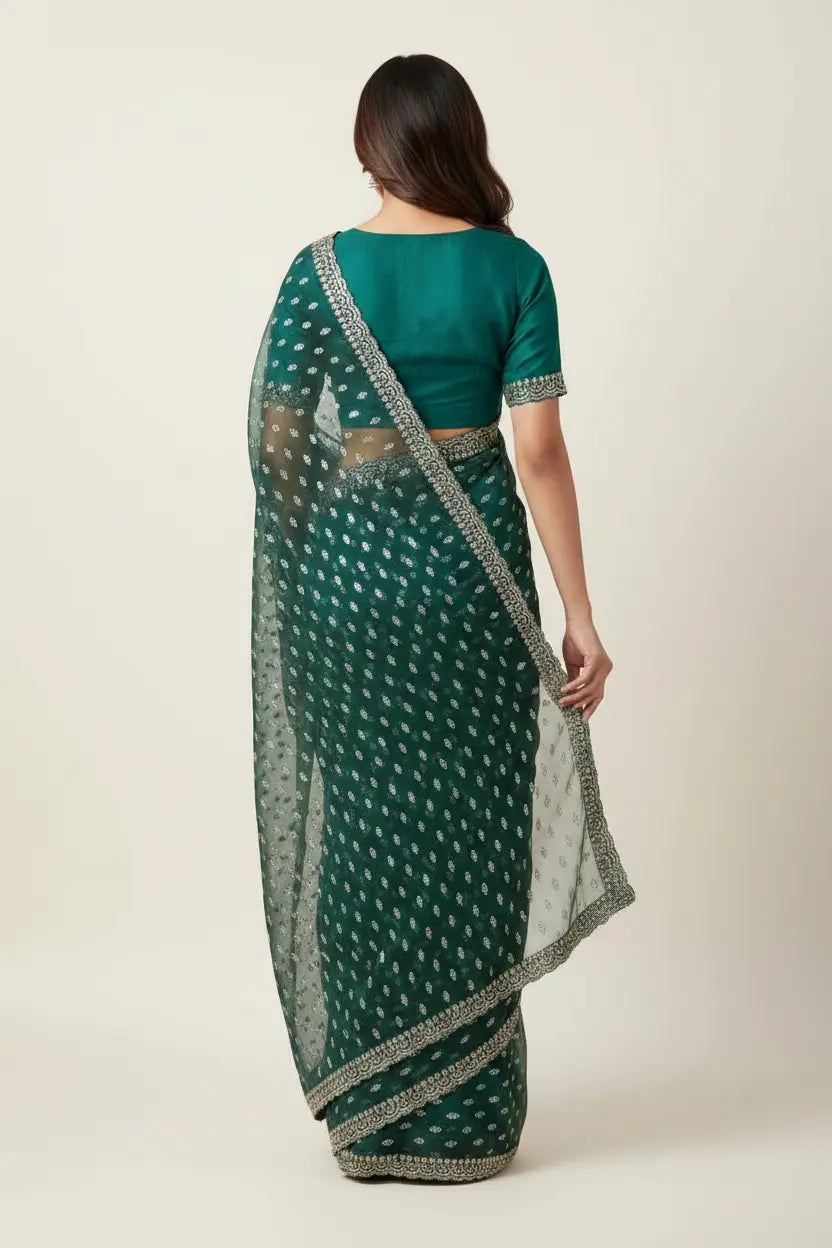 Woman wearing a green saree with a white pattern on a plain background