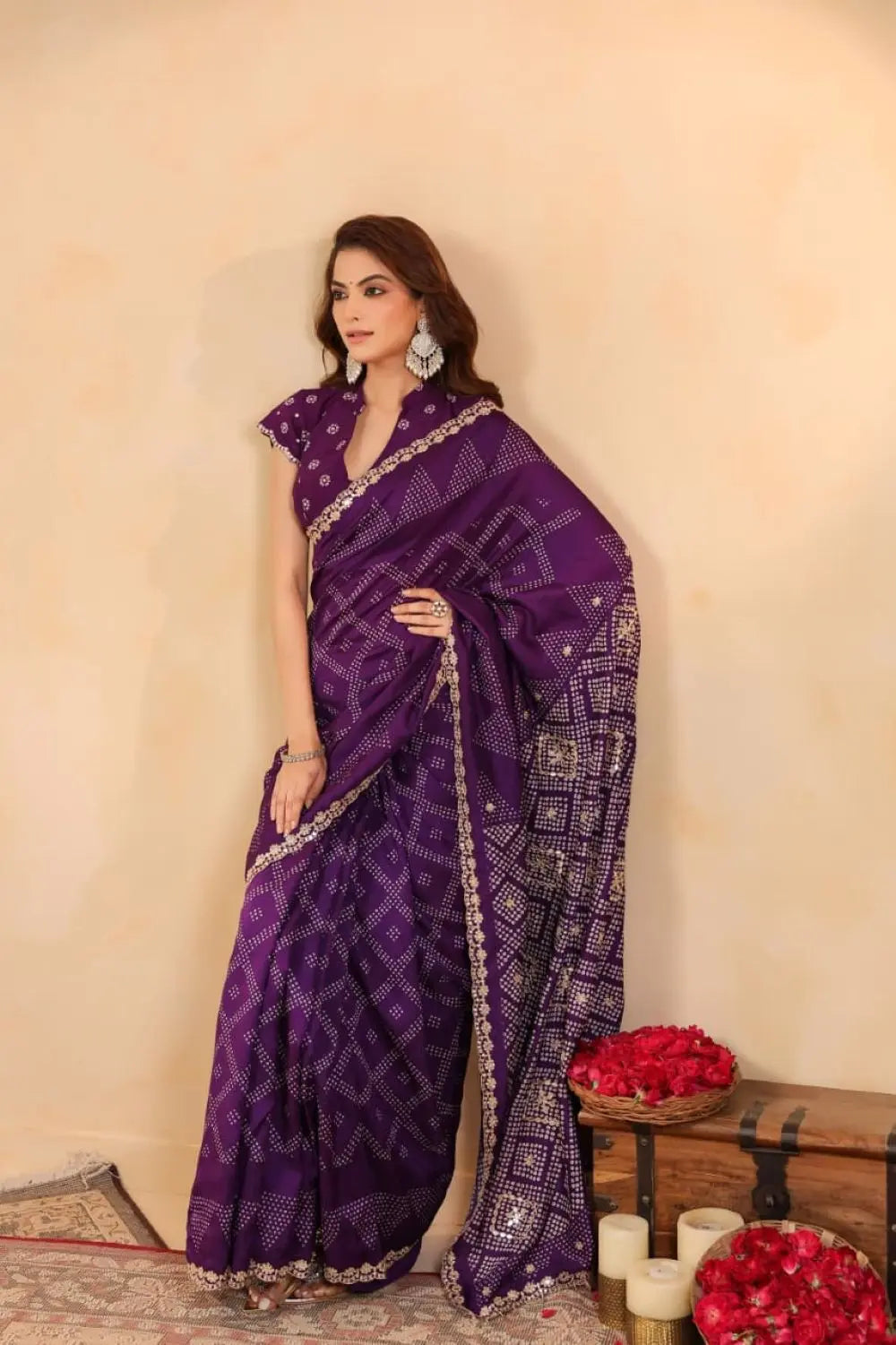 Woman wearing a purple saree with a white pattern against a beige wall.