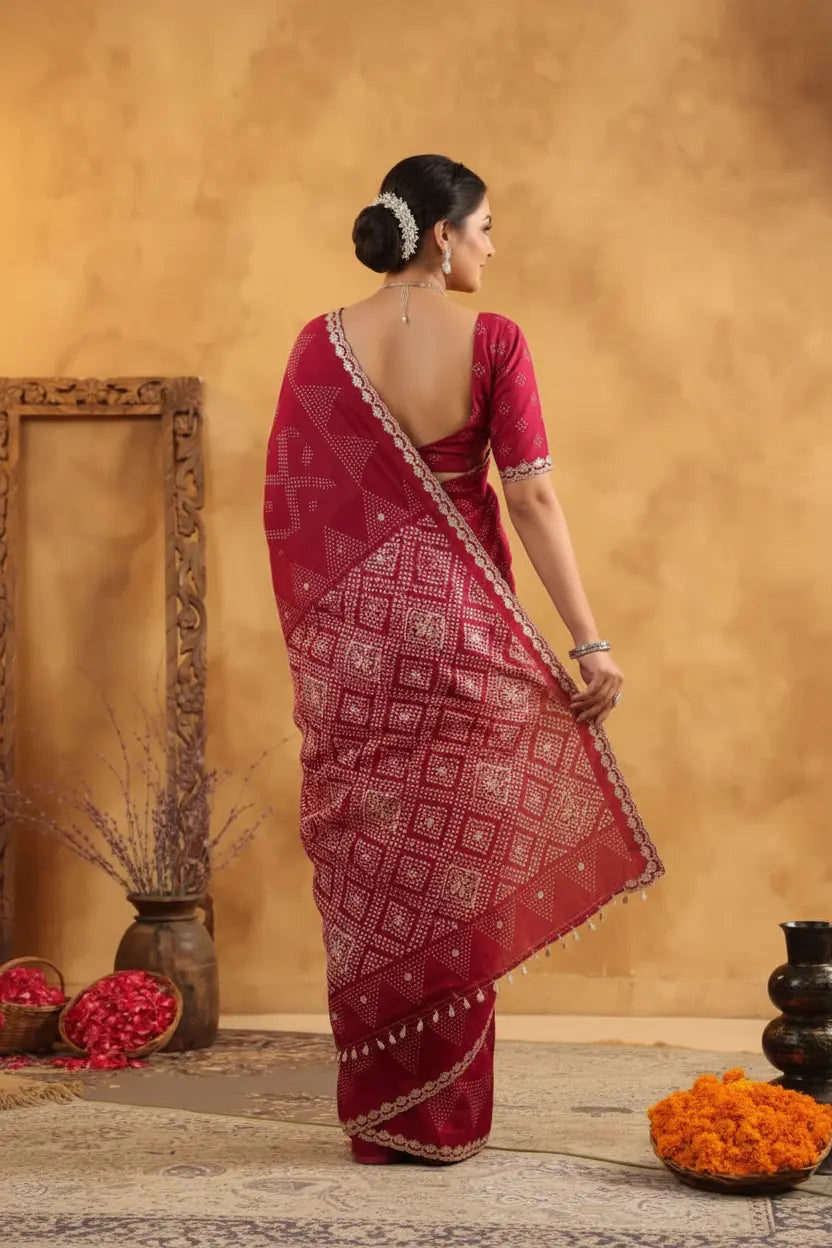 Woman in a red saree with a patterned design, standing against a beige wall with decorative elements.