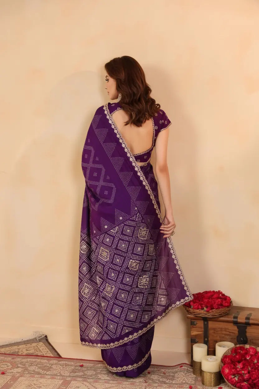 Woman wearing a purple saree with a geometric pattern against a beige wall.