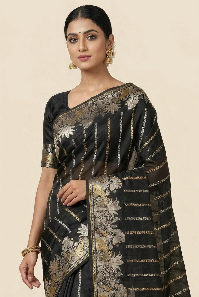 Woman wearing a black saree with gold and white floral patterns on a beige background