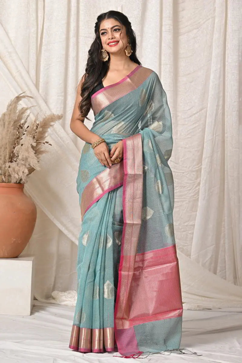 Woman wearing a light blue saree with pink border against a white curtain background