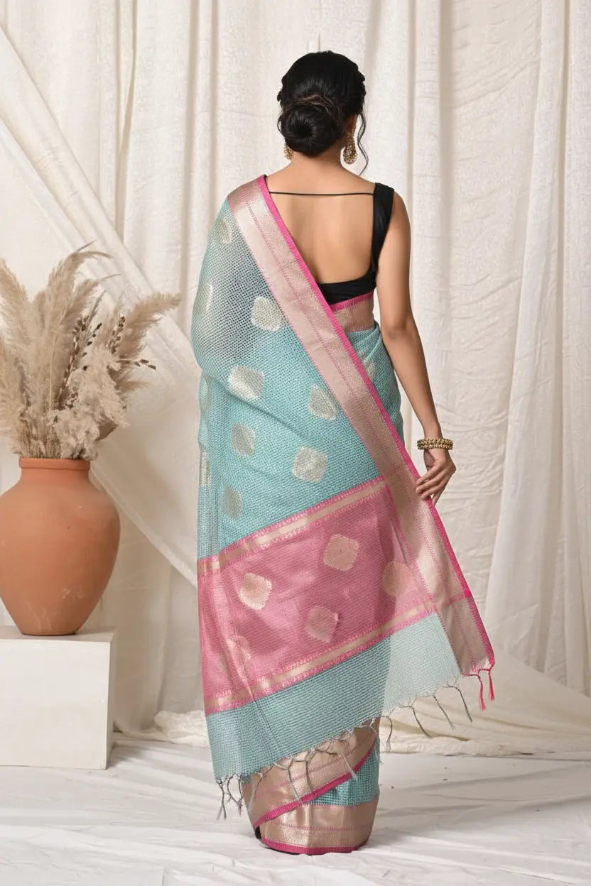 Woman wearing a light blue and pink saree with a white curtain background