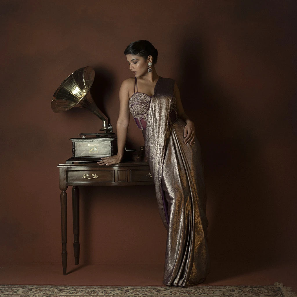 Woman in a long, elegant dress standing next to an old-fashioned gramophone against a brown background
