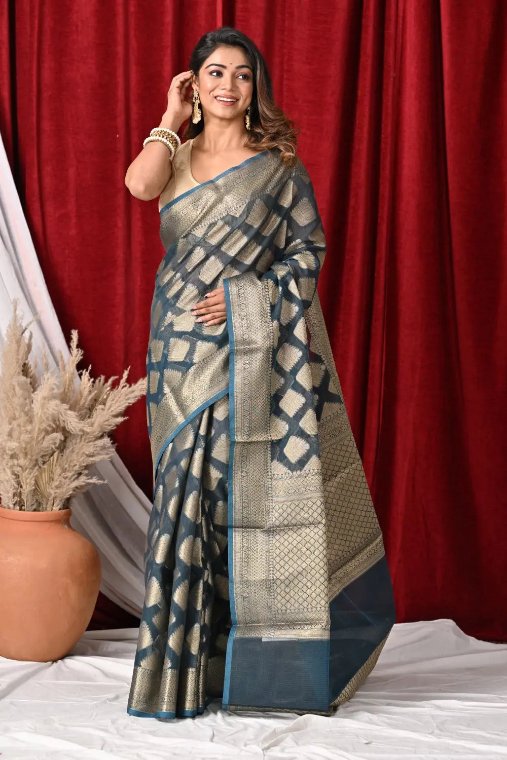 Woman wearing a traditional saree with a geometric pattern against a red curtain background