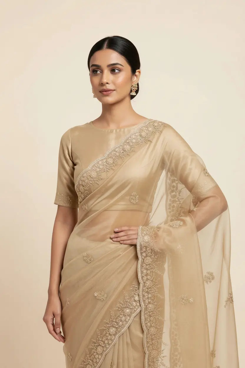 Woman wearing a beige saree with intricate designs on a beige background