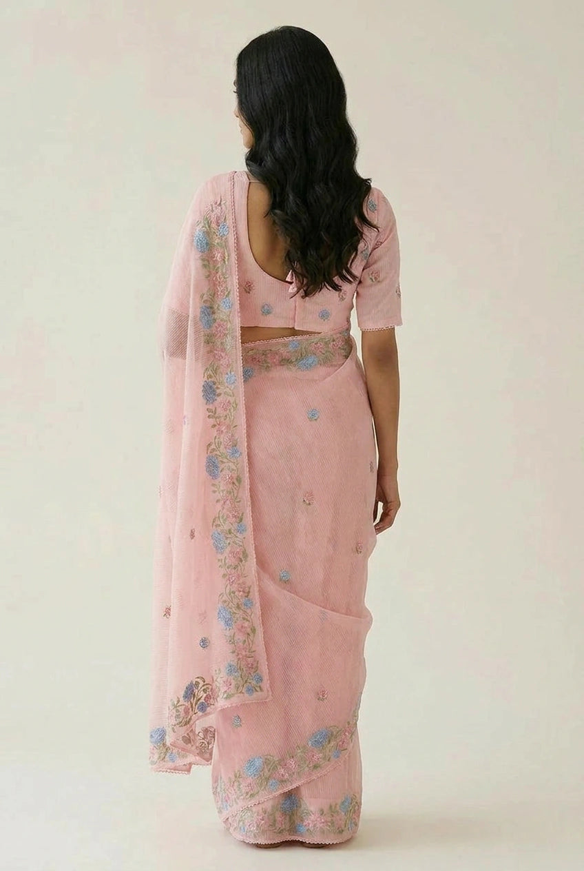 Woman wearing a pink saree with floral patterns on a plain background