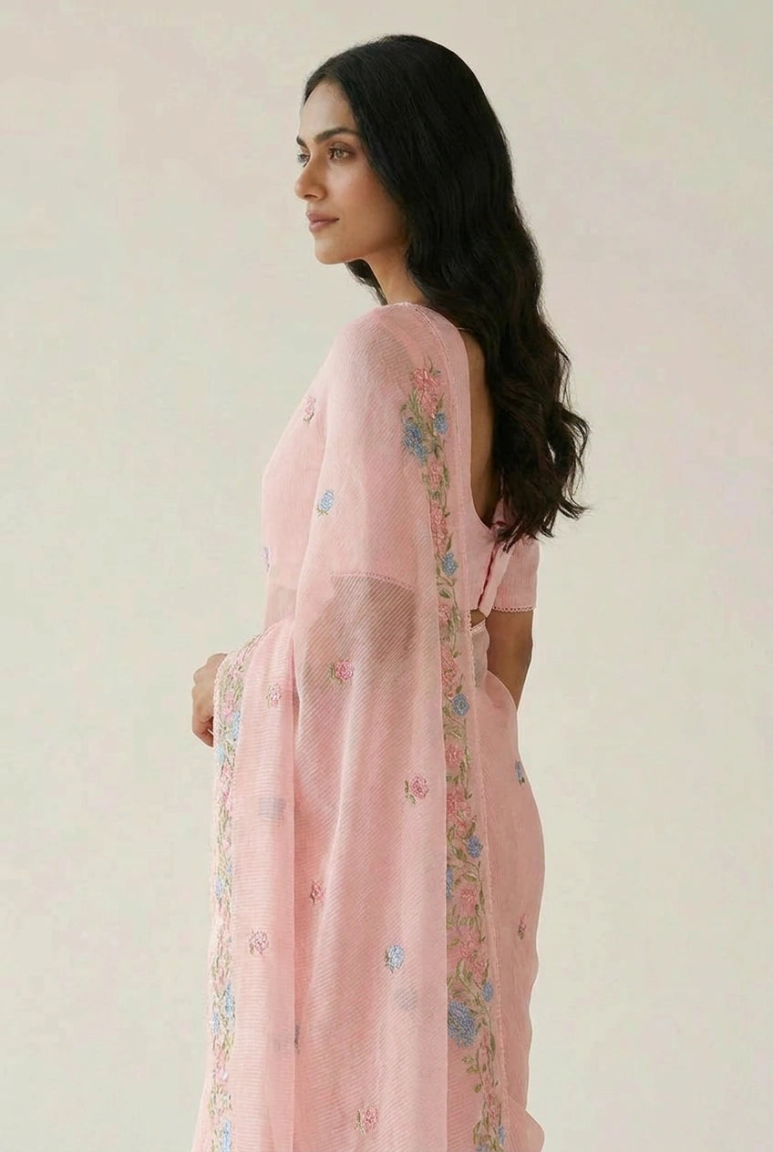 Woman wearing a light pink embroidered outfit against a plain background