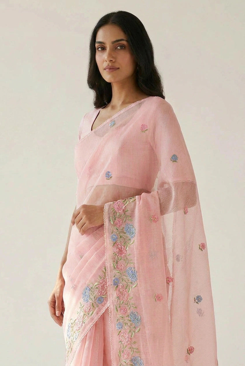 Woman wearing a light pink saree with floral embroidery on a plain background