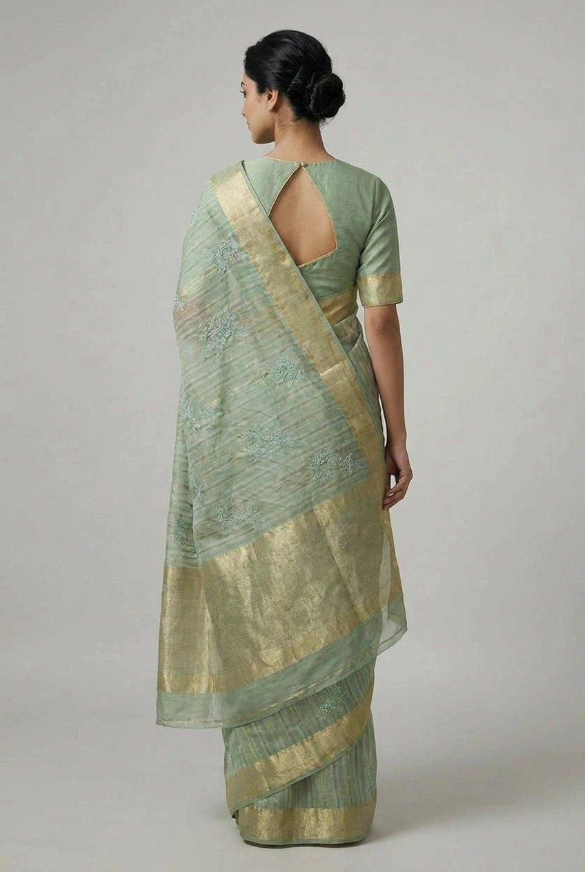 Woman wearing a light green saree with a subtle pattern on a plain background