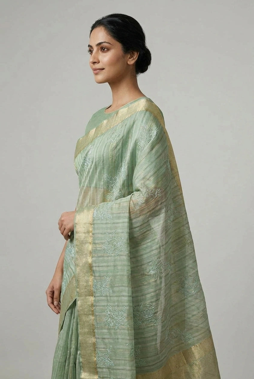 Woman wearing a light green saree with a subtle pattern on a plain background