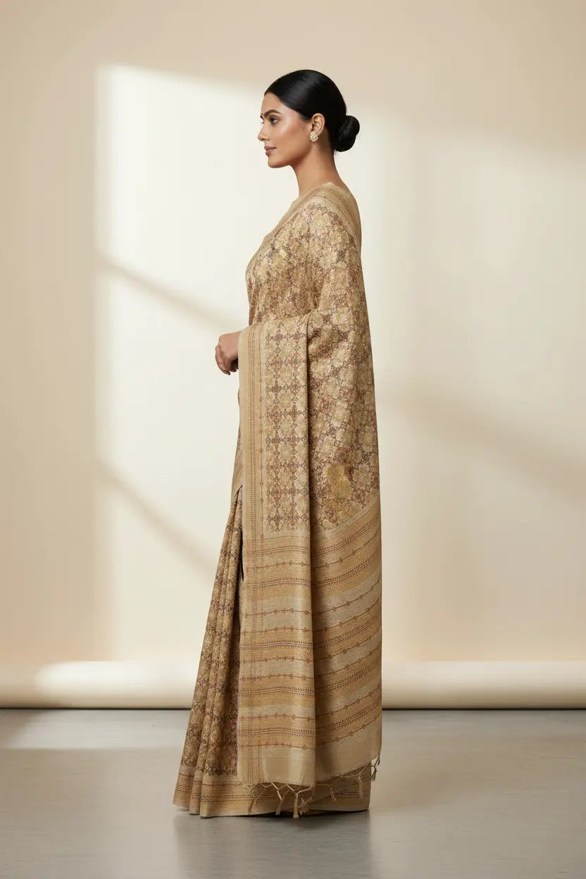 Woman wearing a beige saree with intricate patterns against a neutral background