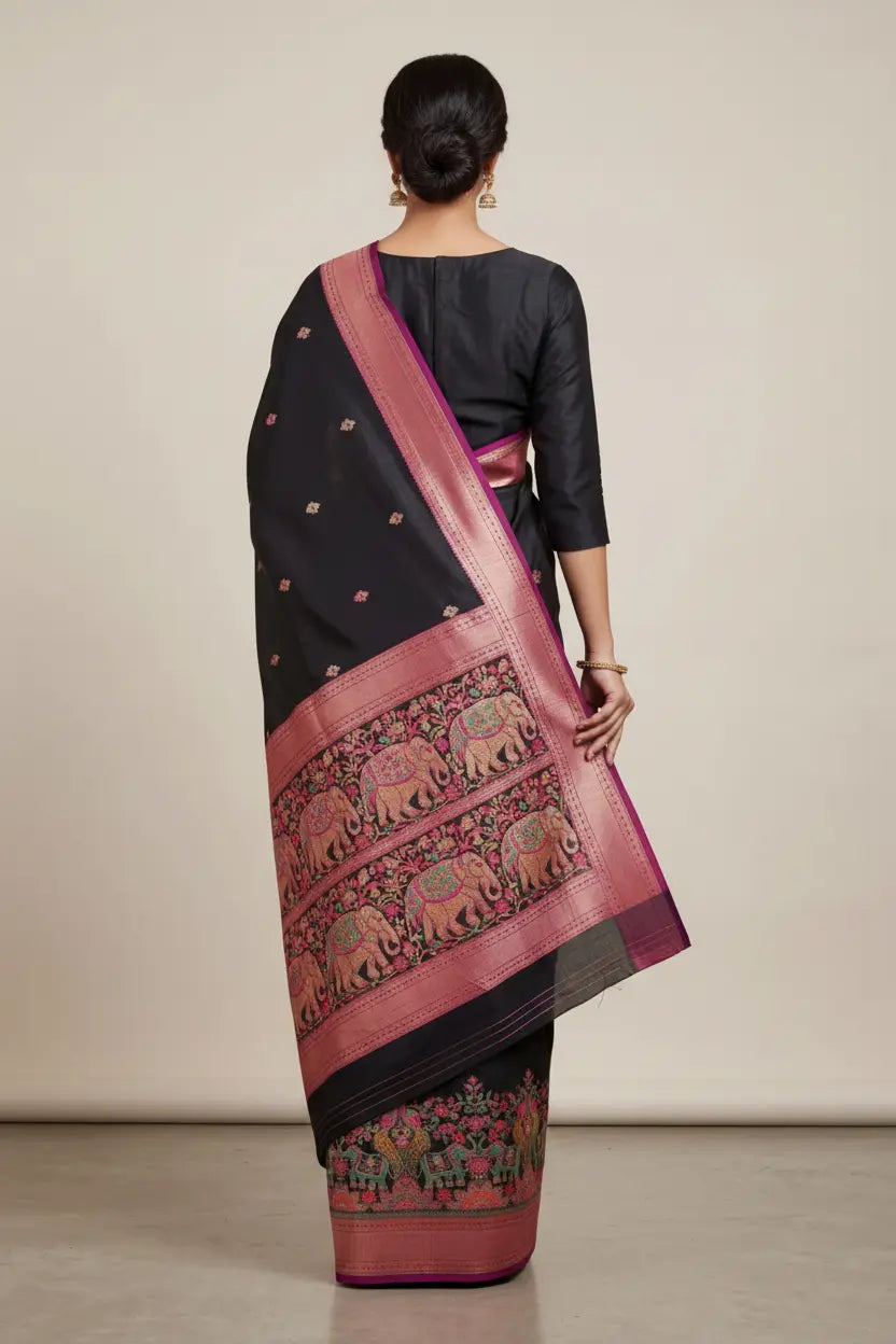 Woman wearing a black saree with pink elephant pattern, standing against a plain background