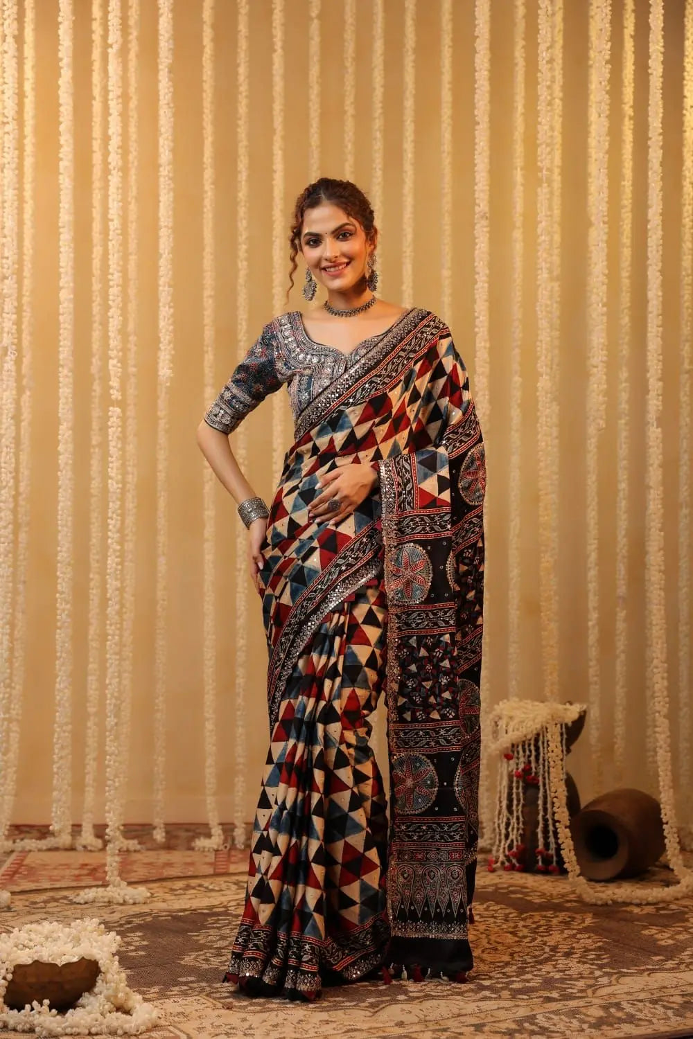 Woman wearing a patterned saree against a textured beige curtain background