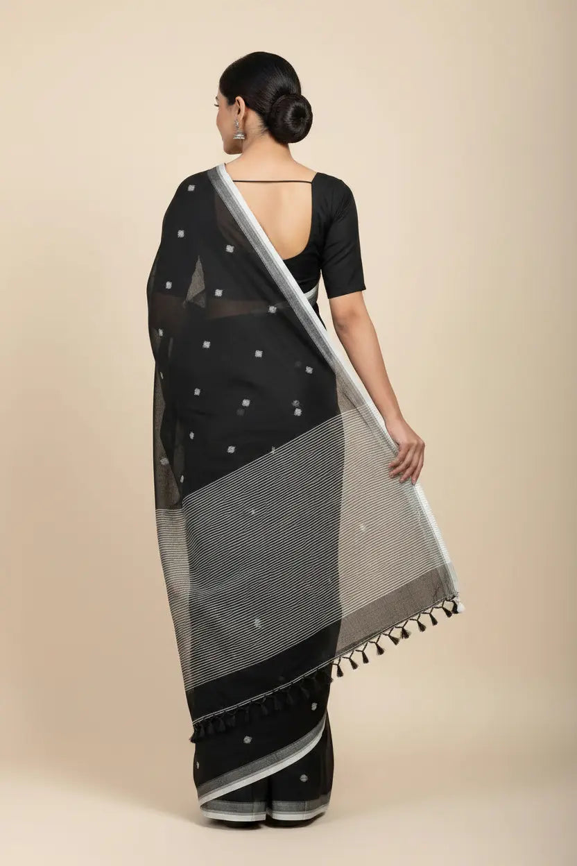 Woman wearing a black saree with a white border on a beige background