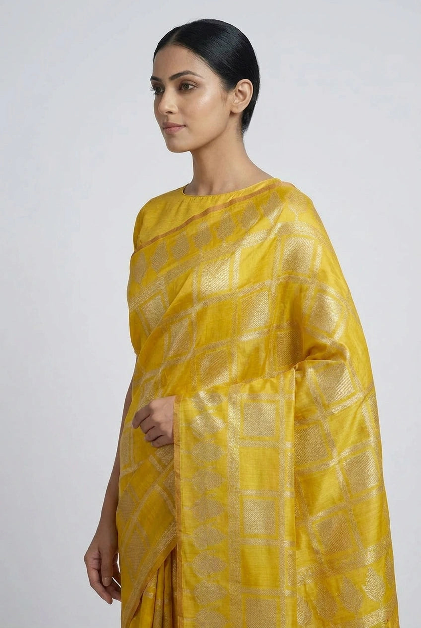Woman wearing a yellow saree with a subtle pattern on a plain background