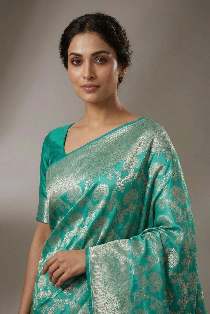 Woman wearing a teal saree with a subtle pattern against a neutral background