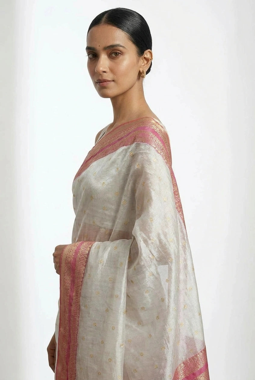 Woman wearing a white saree with pink and gold border on a plain background