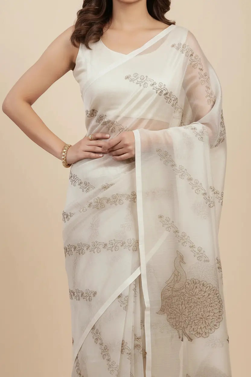 Woman wearing a white saree with intricate gold patterns on a beige background