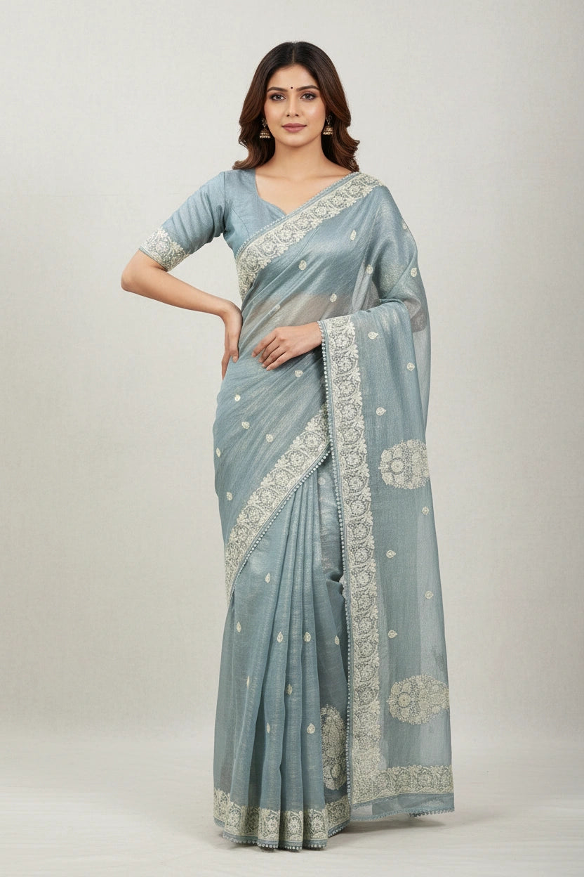 Woman wearing a light blue saree with white patterns on a plain background