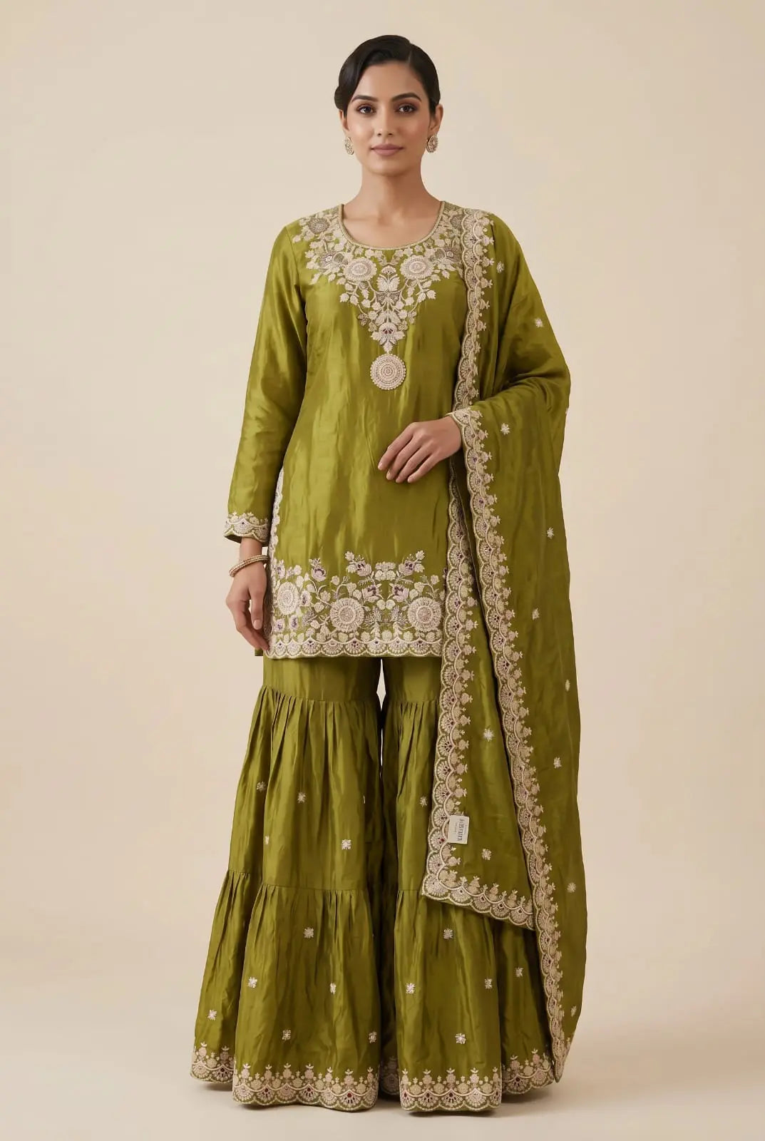 Woman wearing a green traditional outfit with white embroidery on a beige background