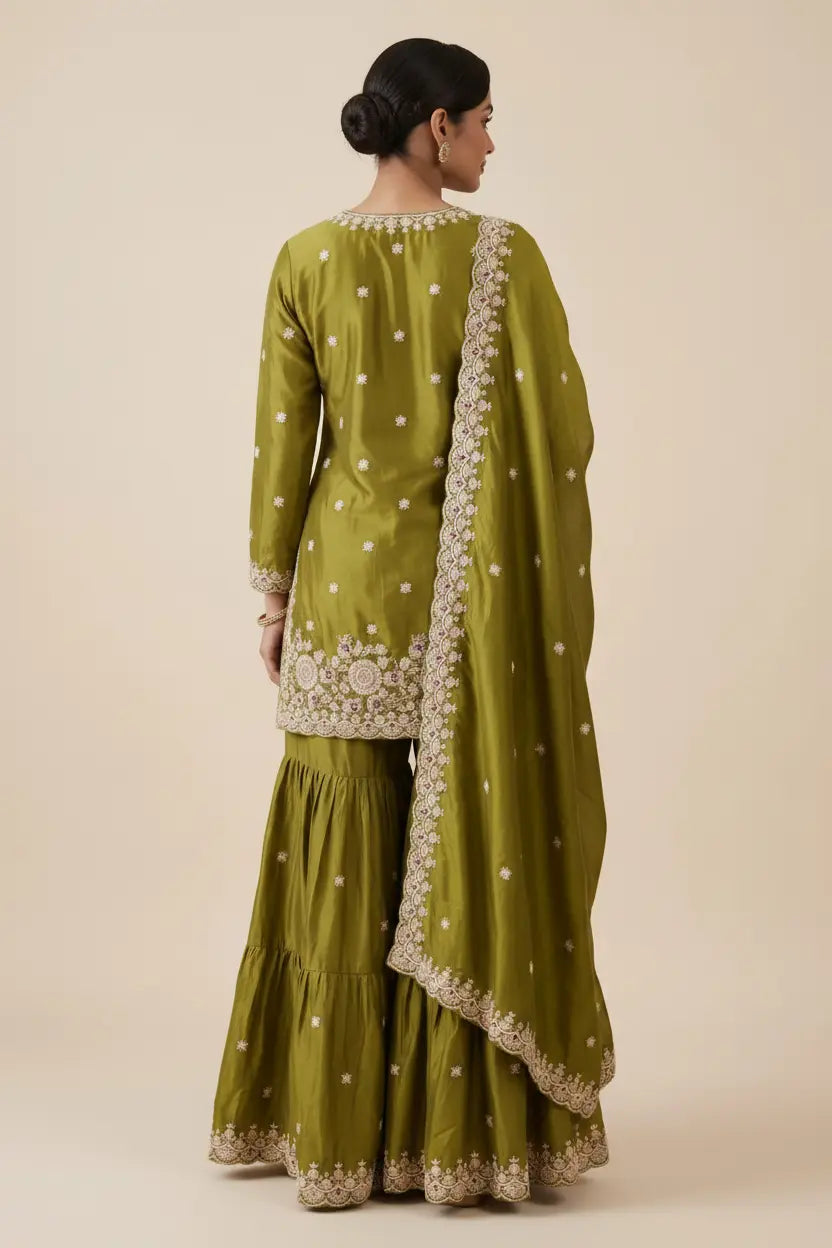 Woman wearing a green traditional outfit with white embroidery on a beige background