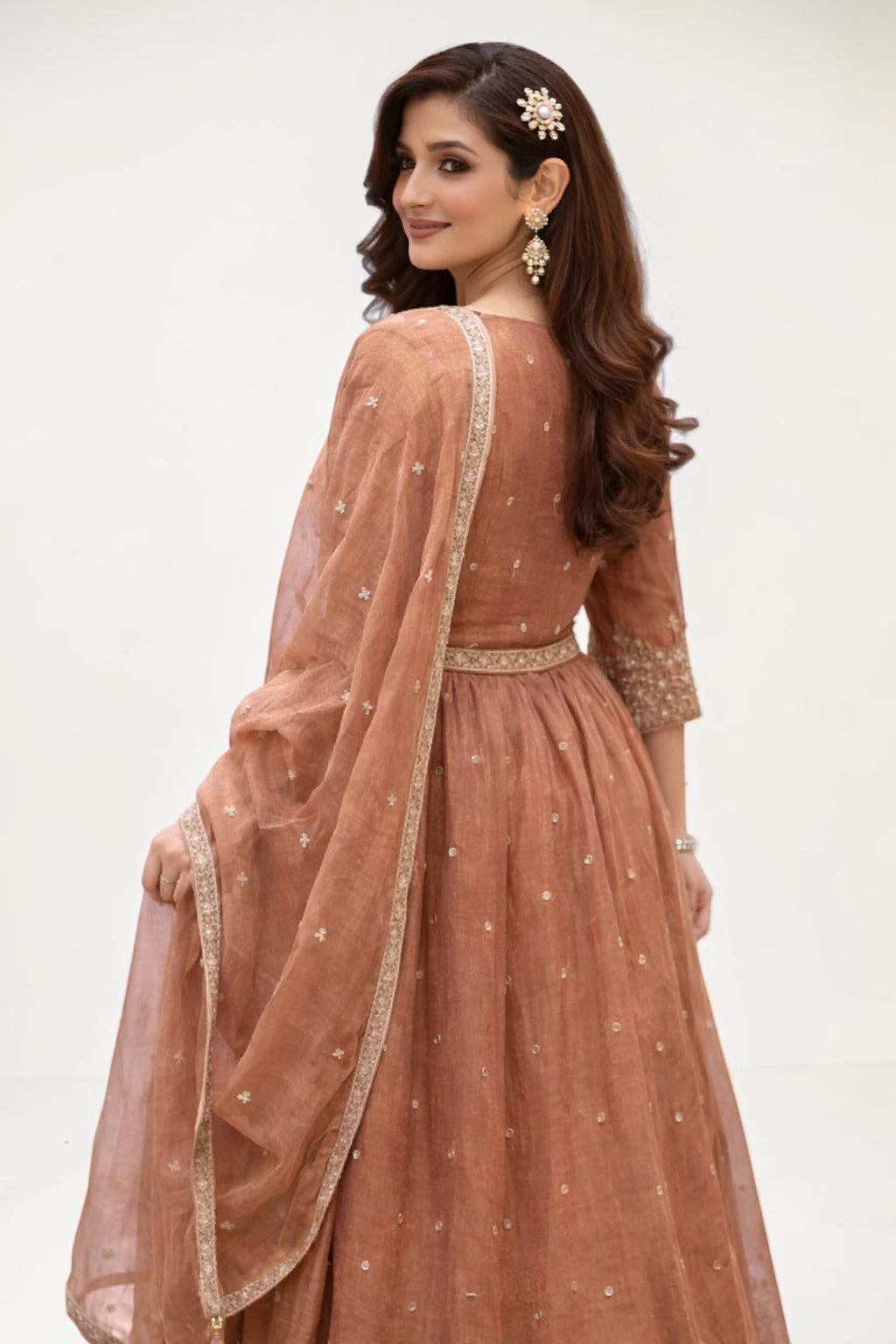 Woman wearing a brown traditional outfit with a sheer dupatta against a white background