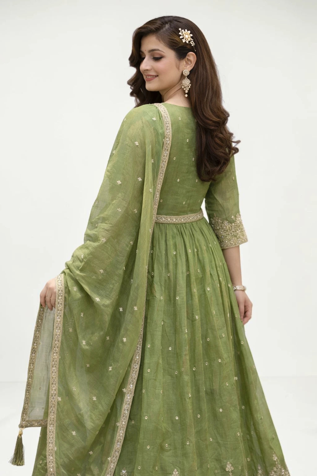 Woman wearing a green traditional outfit with gold embroidery on a white background