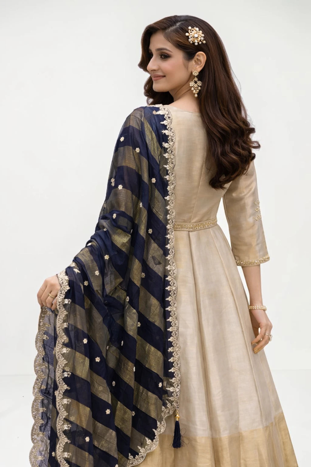 Woman wearing a beige dress with a navy blue and gold dupatta on a white background
