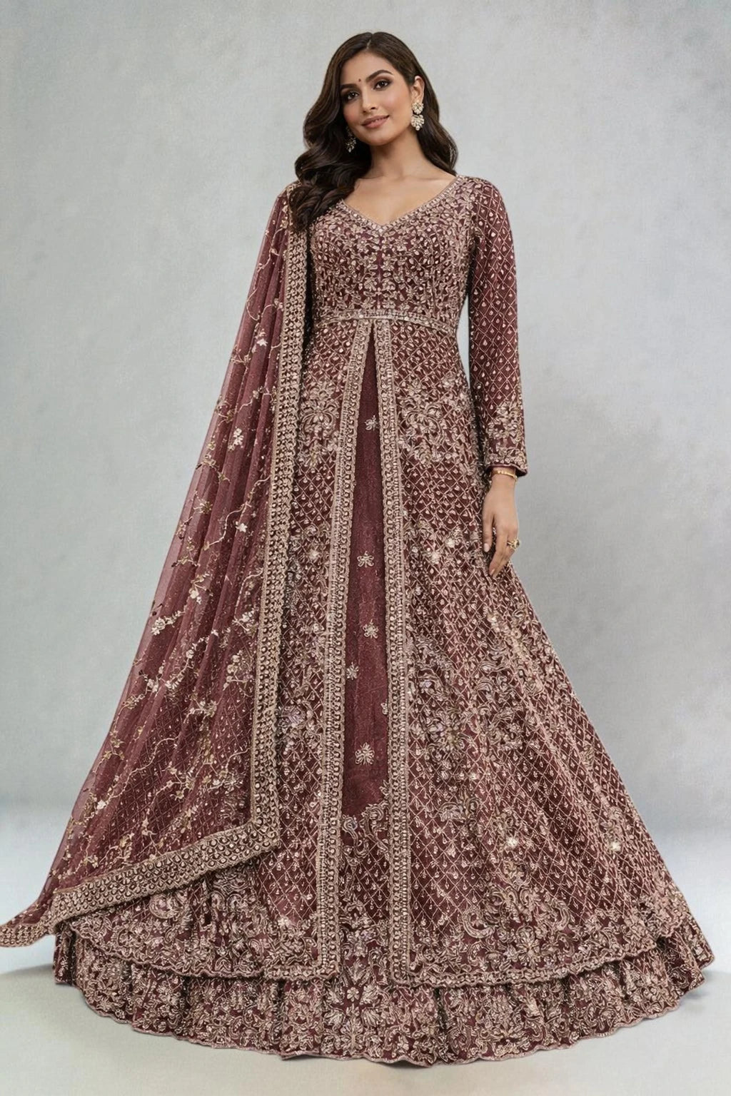 Woman wearing a brown embroidered traditional outfit with a dupatta on a plain background