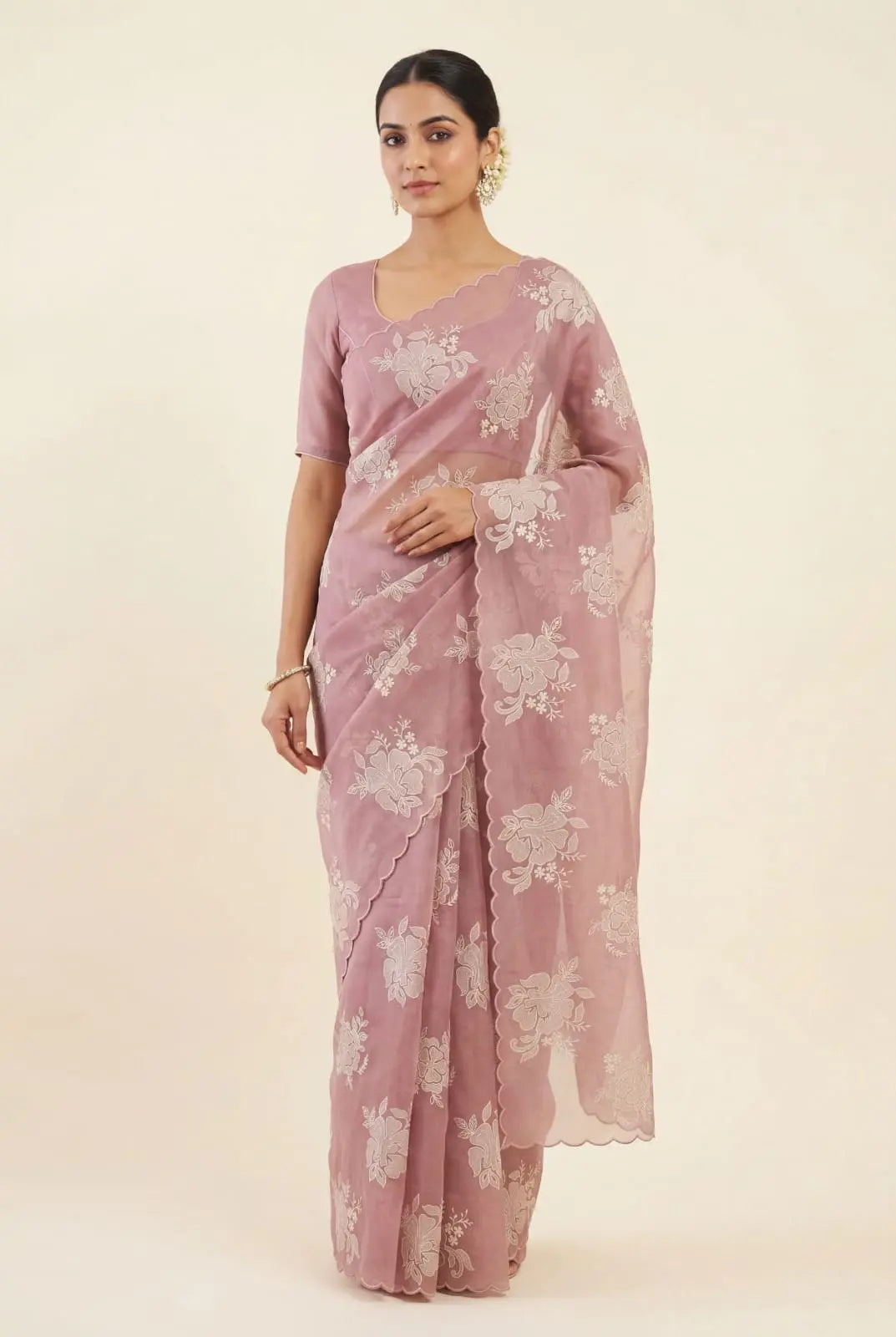 Woman wearing a pink saree with white floral patterns on a beige background