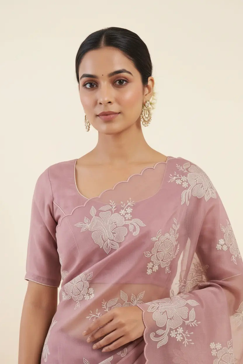 Woman wearing a pink saree with white floral embroidery on a beige background