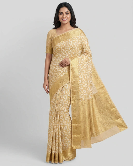 Woman wearing a gold saree with a white blouse on a gray background