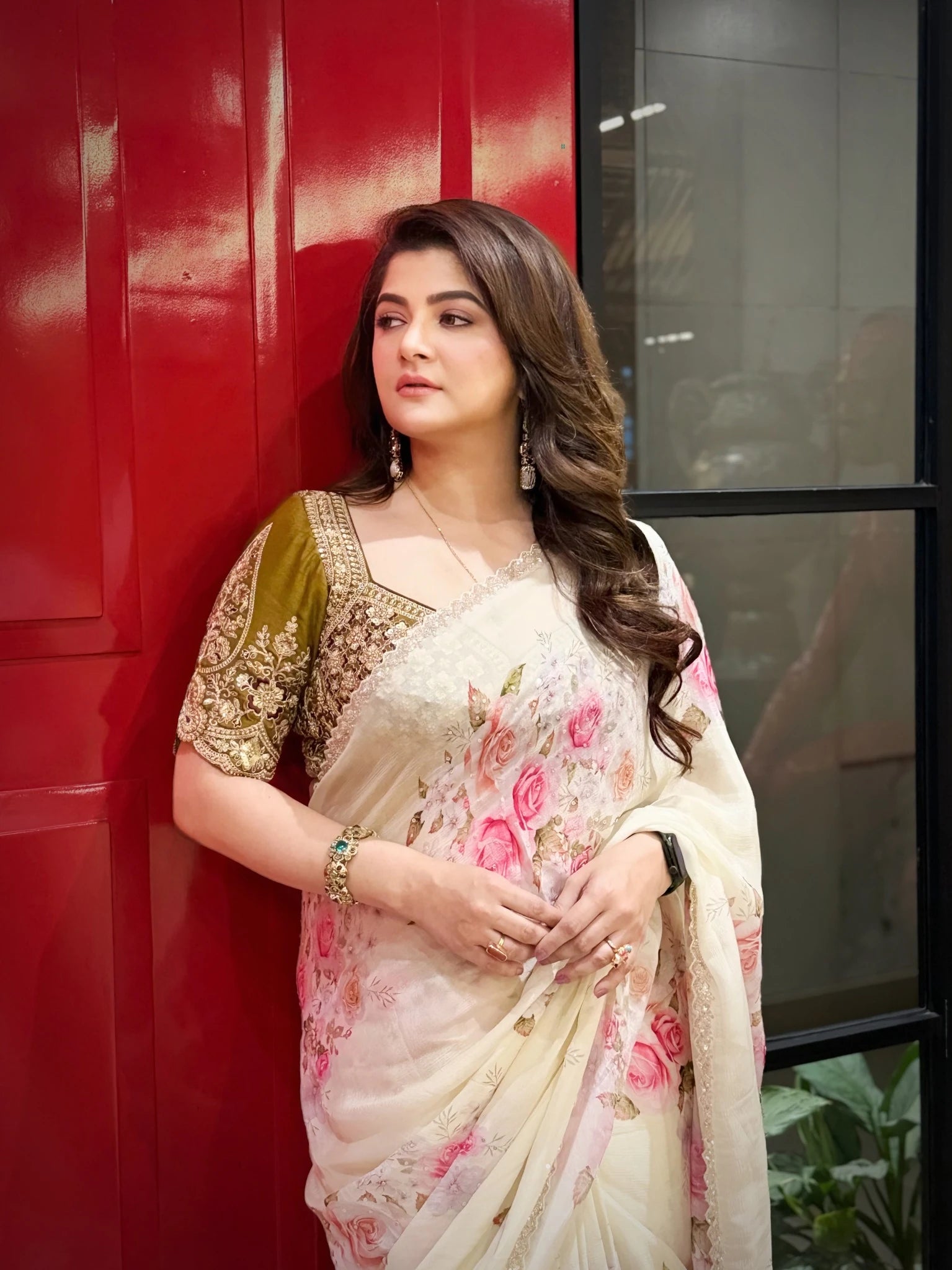 Woman in a floral saree standing against a red wall.