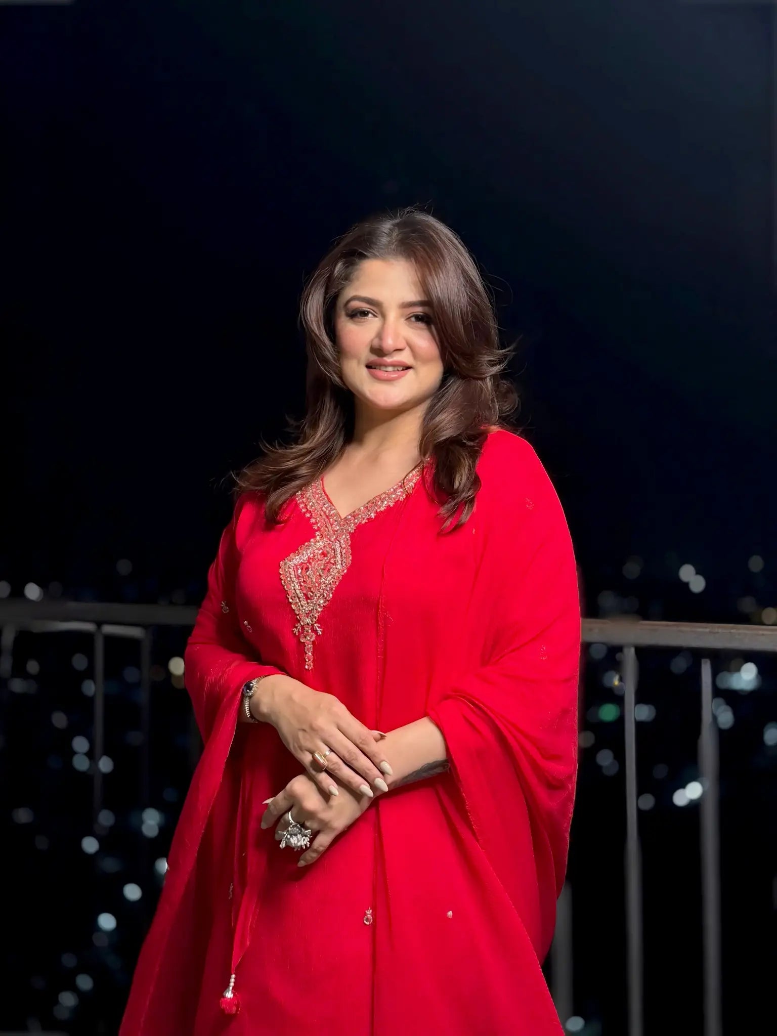 Woman in a red traditional outfit with intricate designs against a dark background
