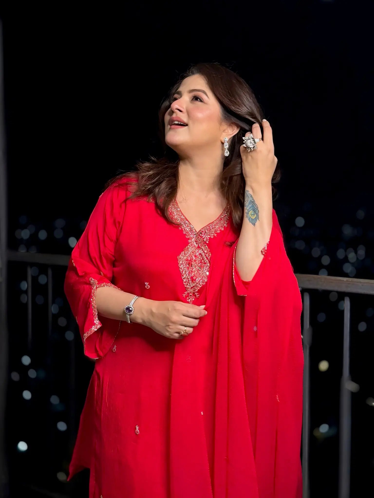 Woman in a red traditional outfit with intricate designs, standing against a dark background.
