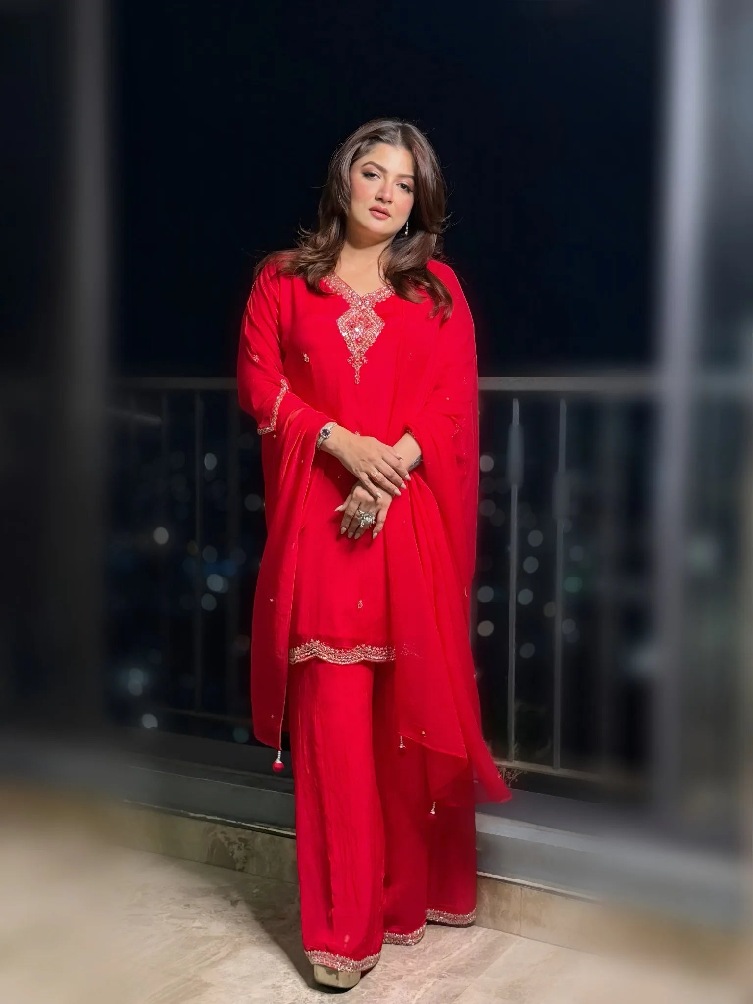 Woman wearing a red traditional outfit with intricate designs against a dark background.