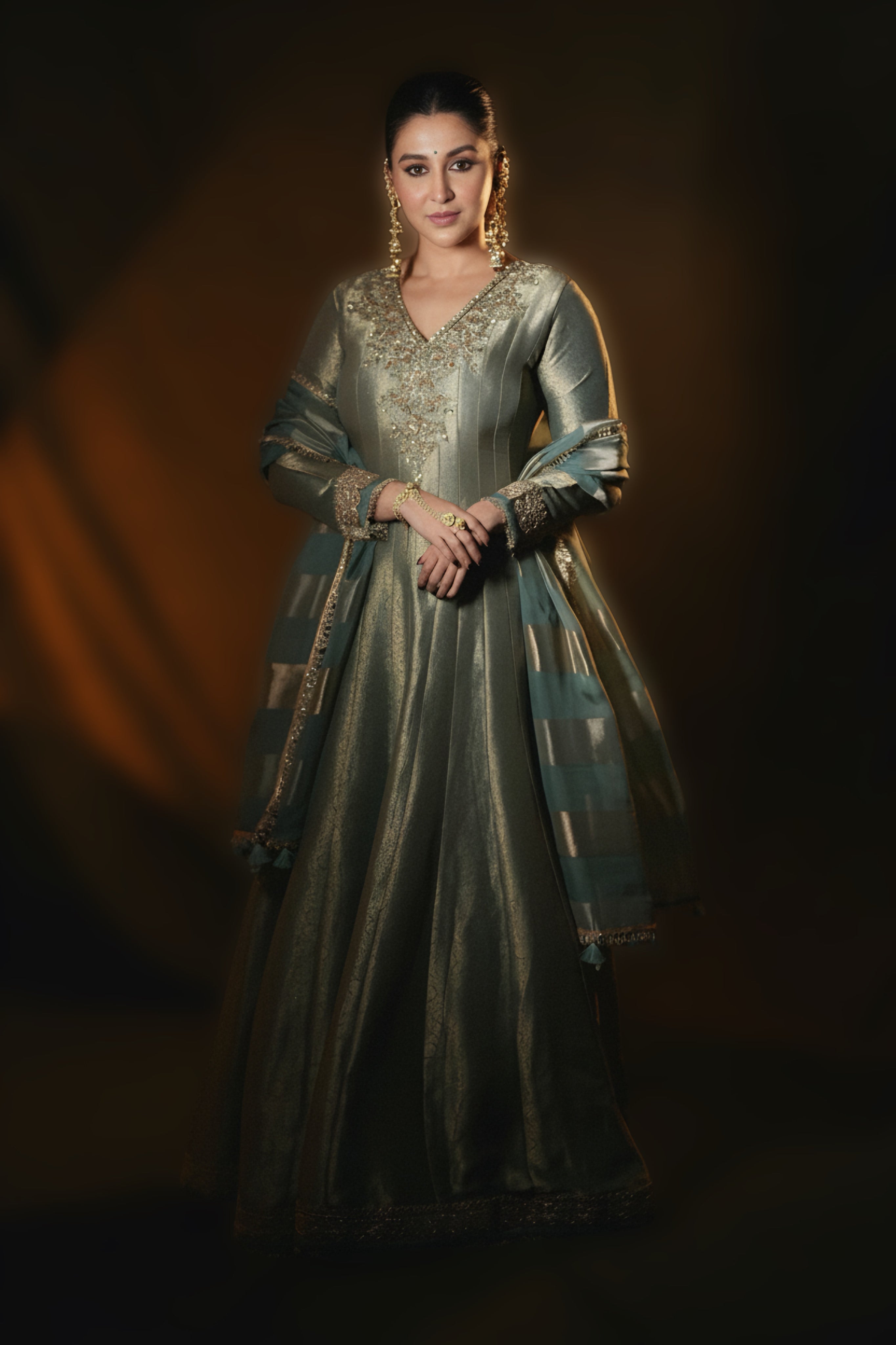 Woman in a traditional green and gold outfit against a dark background
