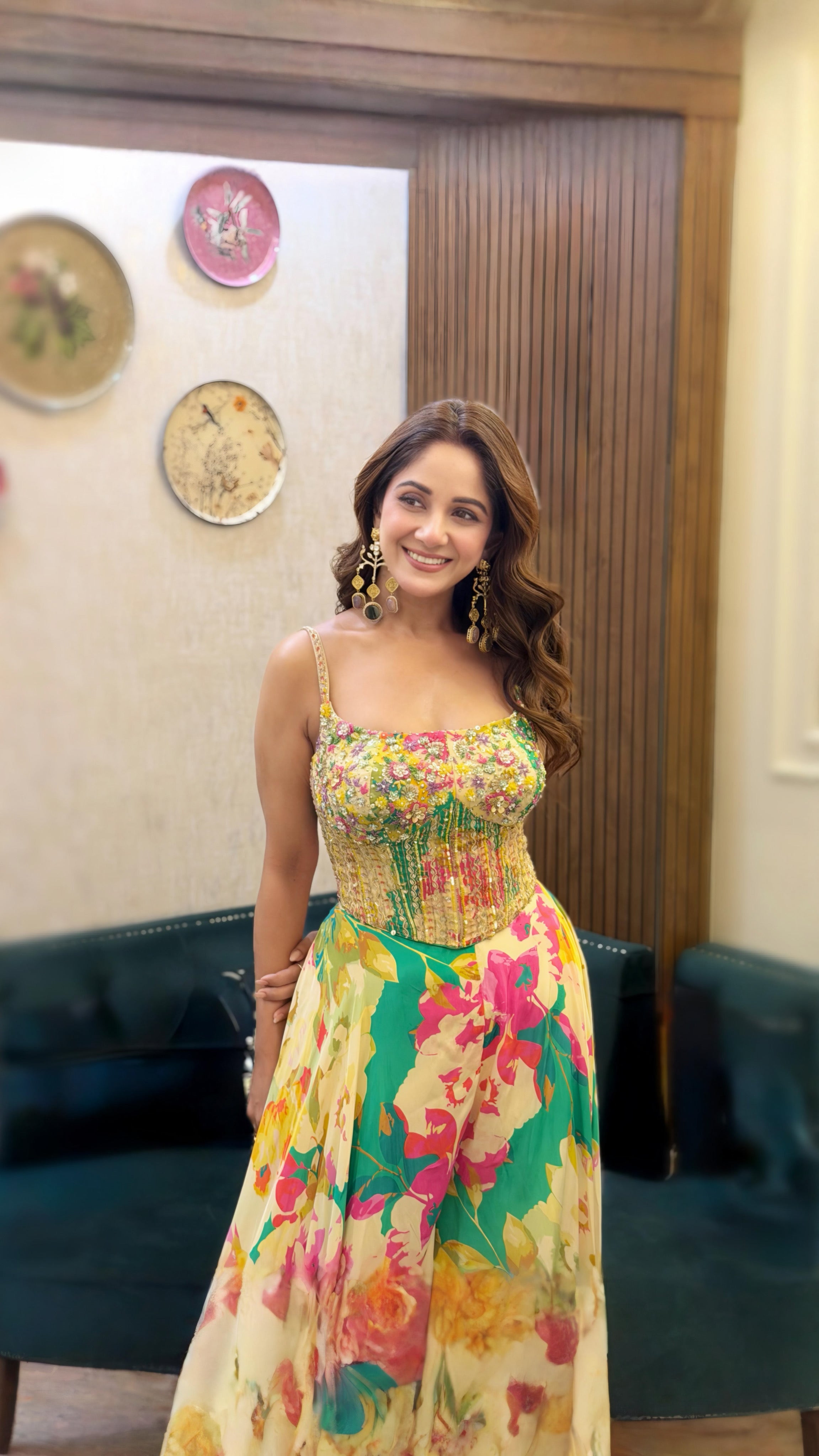 Woman in a colorful floral dress standing indoors with decorative plates on the wall.