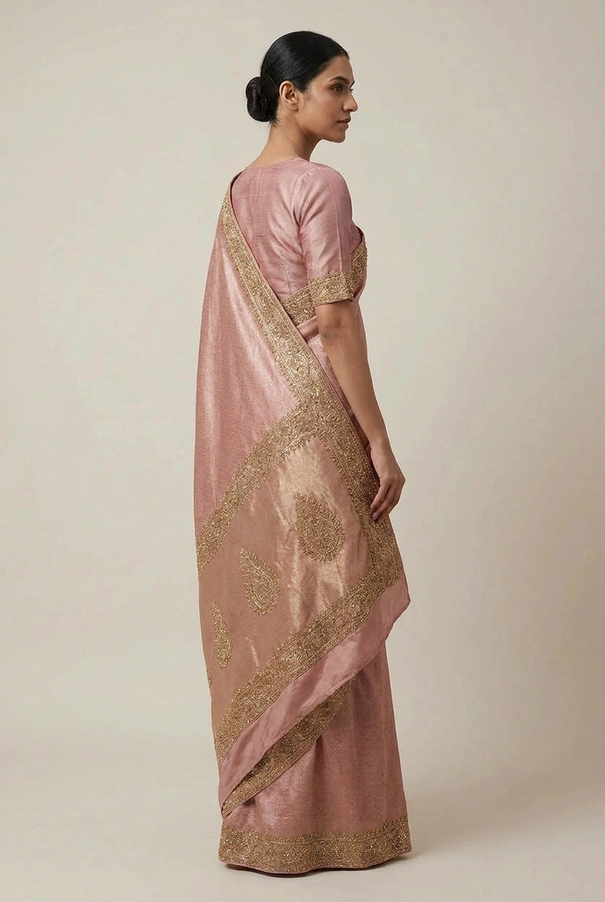 Woman wearing a pink saree with gold embroidery on a beige background