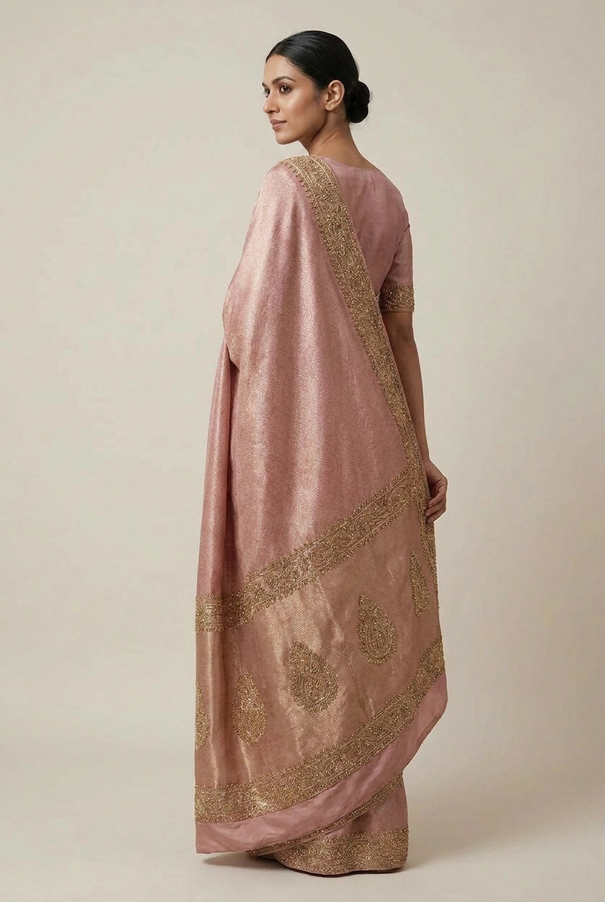 Woman wearing a pink saree with gold embroidery on a beige background