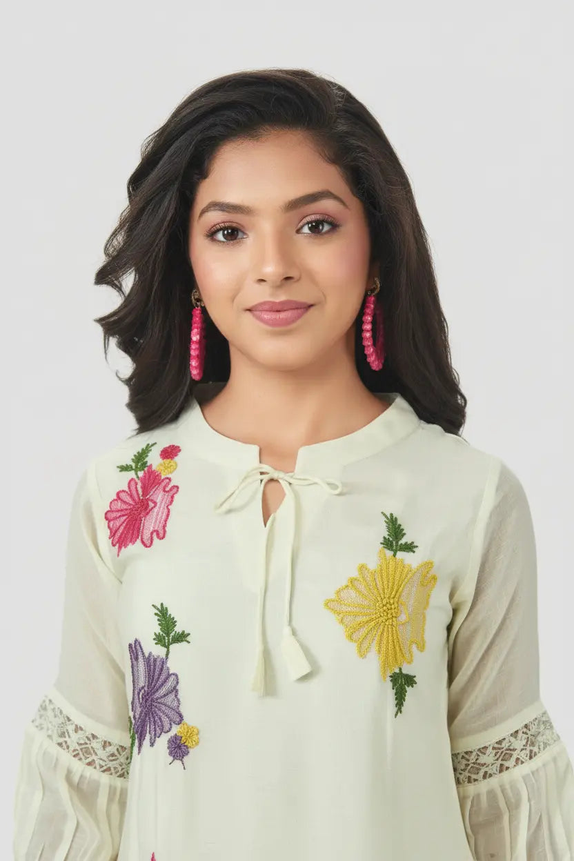 Woman wearing a white embroidered top with colorful flowers on a plain background