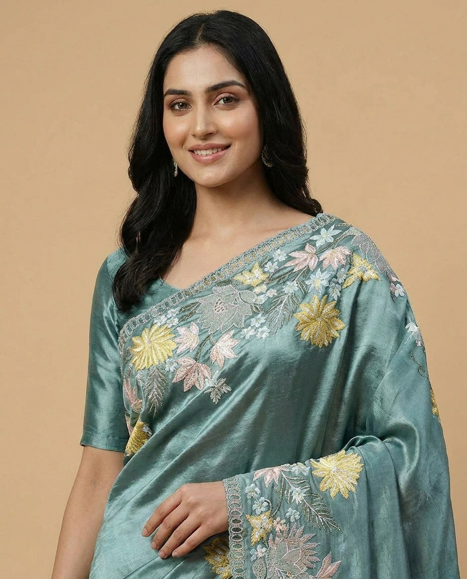 Woman wearing a teal saree with floral embroidery on a beige background