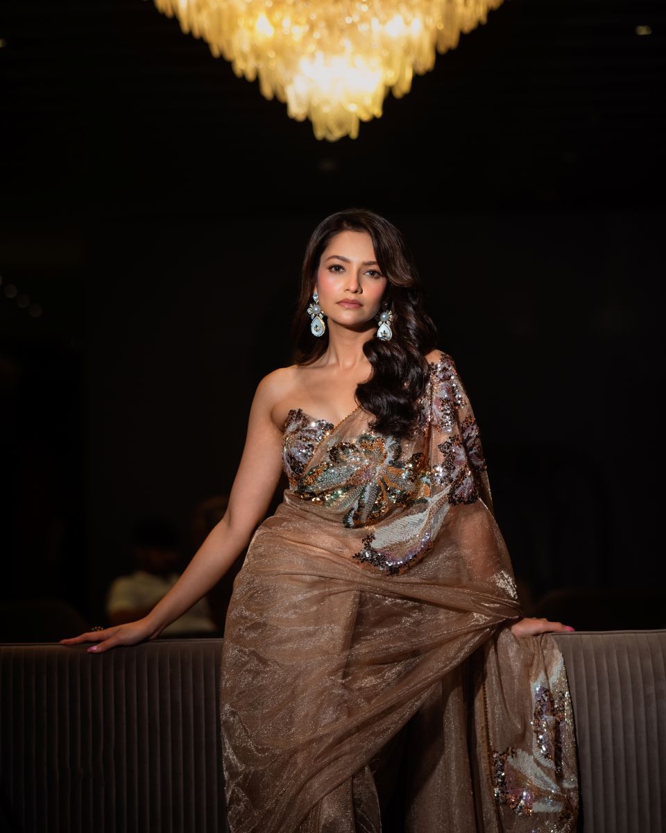 Woman in a sparkling dress posing indoors with a chandelier in the background