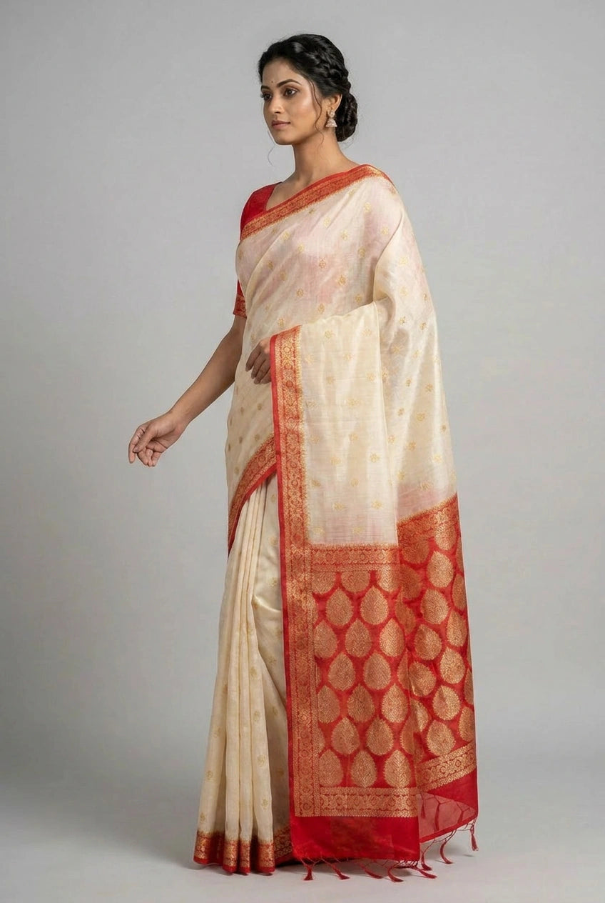 Woman wearing a traditional cream saree with red border on a gray background
