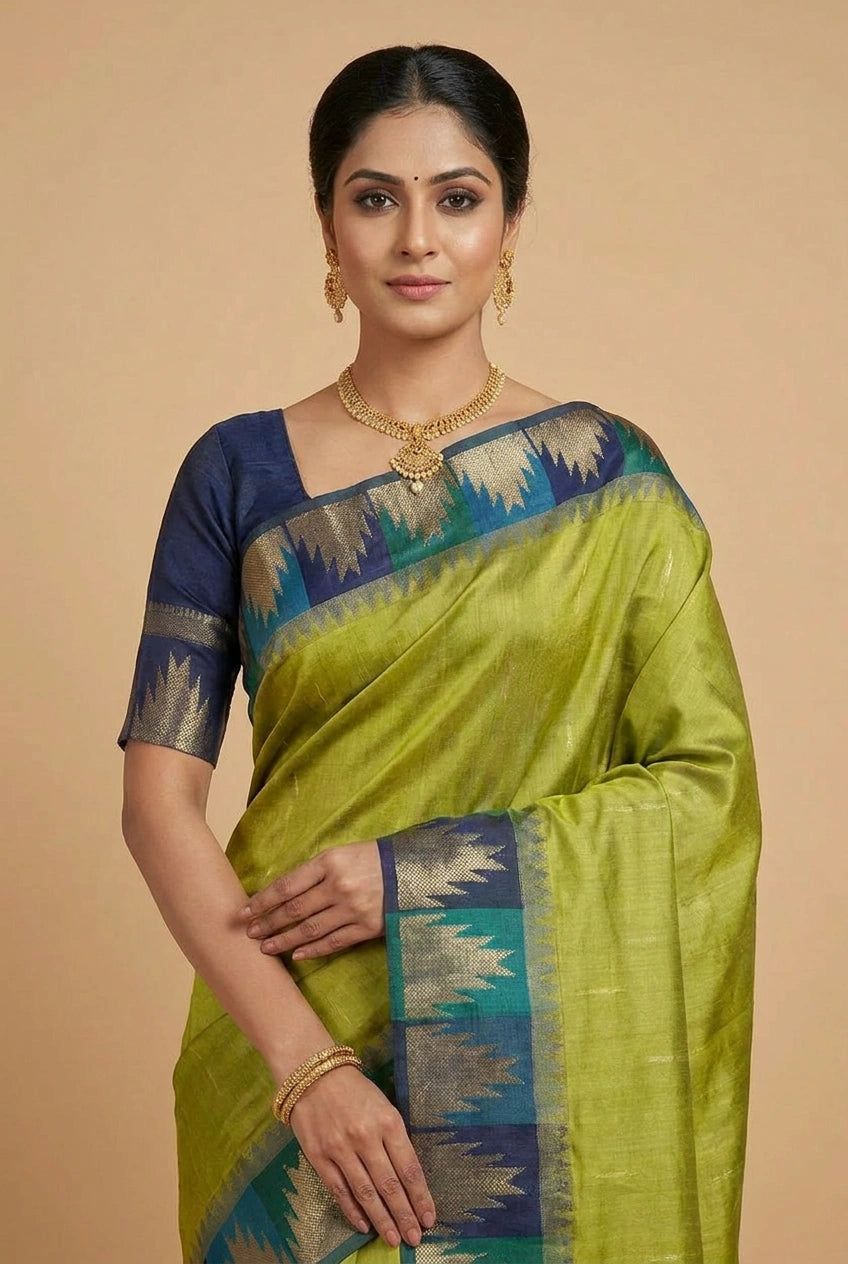 Woman wearing a green saree with blue and gold border on a beige background